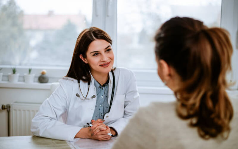 Picture of a smiling female doctor sitting at a desk and looking a patient.